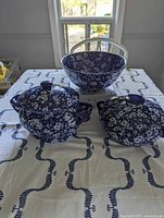 Image showing three pieces of blue and white calico cherry blossom patterned serving ware on a white cloth with blue pattern. Includes one open bowl and two lidded serving dishes.