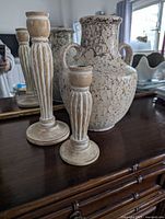 Full view of vase and two wooden candlesticks on a dark wooden surface with mirror behind.