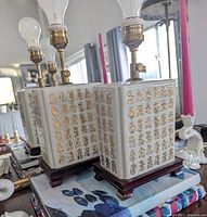 Pair of vintage chinoiserie table lamps displayed side by side, showing the porcelain bodies with gold calligraphy and wood bases