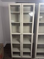 Front view of tall white cabinet with two glass doors revealing multiple shelves inside.