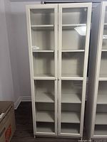 Front view of the white cabinet showing two glass paneled doors and shelves inside