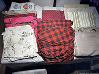 Overview of all items including multiple folded curtains, rugs, blankets, and a beige bag with circular handles.