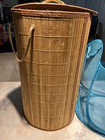 Cylindrical woven bamboo style laundry bin with rope handles, shown standing upright.