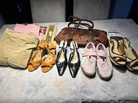 Full view of the brown purse, four pairs of shoes, and two skirts laid out on a table