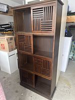 Front view of the wooden shelving unit showing three sliding doors with geometric slatted design and three open compartments.