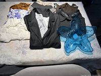 Blue glass starfish platter in front of folded assorted clothing including blazers, knit tops, and blouses.