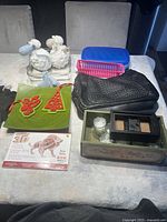 Full view of the lot items on table including stuffed sheep toys, decorative votives, black purse, plastic containers, green plate with decorations, and wooden puzzle kit.