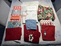 Photo showing all nine assorted tea towels laid out on a table, including new packaged towels and various holiday themed towels.