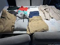 Overview of all garments laid on a bed, showing jackets, sweatshirts, pants, and jeans in various colors.