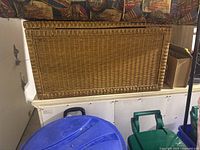 Front and top view of rectangular wicker trunk placed on white cabinet with a colorful cloth hanging above.