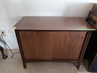 Front view of small wooden cabinet with sliding doors and round recessed handles.