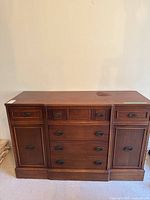 Front view of the wood cabinet showing the entire piece with multiple drawers and doors, displaying its medium-dark wood finish and brass oval drawer pulls.