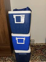 Stack of three blue Coleman coolers with white lids and handles, showing size and color variations.