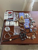Overview photo showing assortment of costume jewelry including bracelets, watch, brooches, and earrings on a wooden table.