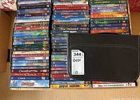 Full view of the Disney DVD collection arranged in three vertical stacks next to a black zippered DVD storage case on a light brown surface