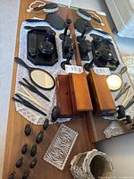 Overview of ebony vanity set components arranged on wooden table with doily, including mirrors, brushes, ink set, candlesticks, jewelry box, decorative glass tray, and small wooden decor items.