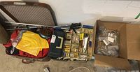Overview of multiple tackle boxes, fishing rod parts, yellow rain gear, a fishing reel, and a metal case.