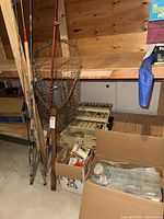 Wide view showing fishing rods leaning against workbench, landing net behind, tackle box and lure box on floor