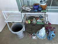 Wide view of all garden decor items showing metal plant stand, pots, various small garden accessories, Buddha statue, blue fairy figurine, and pink glass candle holders