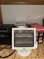 Front view of three portable heaters: white NOMA heater in front, black heater with digital display behind on left, Honeywell heater box on right.