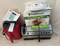 Photo showing Dash red air fryer, FoodSaver vacuum sealer, and FoodSaver box with sealing supplies