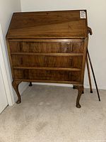 Full view of the wooden secretary desk with three drawers and three walking canes standing next to it.