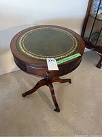 Full view of round wood side table with green leather and gold border top, showing drawer and tripod base with claw feet.