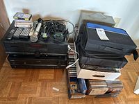 Overview of the stereo equipment on hardwood floor next to a wall showing cassette deck, receiver, microphone, remotes, cables, and many CDs in boxes.