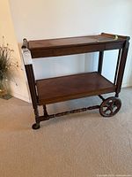 Full view of wooden tea trolley showing two-tier shelves, large spoked wheel, and smaller caster wheel.