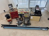 Wide view of all items in the lot arranged on floor, showing movie editor/viewer, developing tank, video transfer system, projectors, camera, tripod screen, reels and accessories.