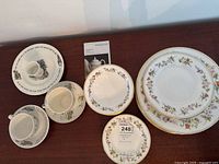 Wide view of mixed Wedgwood Mirabelle china plates, Bunnykins cups, and saucers arranged on wooden surface with a Wedgwood booklet visible.