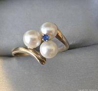 Front and top view of the ring showcasing three pearls and one small blue gemstone on a yellow gold band.