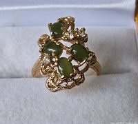 Front view of gold plated ring with four green stones and four clear stones in ornate setting