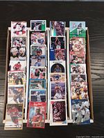 Boxes of assorted sports trading cards from hockey, baseball, football, and basketball shown upright, displaying various cards with colorful front designs, player images, and team logos.