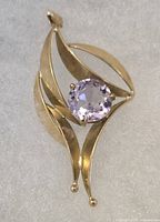 Front view of the 9Kt gold pendant showing its abstract curved design and central round faceted purple stone.