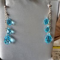 Front view of the pair of silver dangle earrings with three blue crystal drops each, displayed on a gray background.