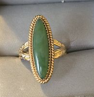 Front view of elongated oval green stone set in gold tone bezel with twisted rope edge and decorative band