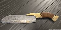 Full view of large Damascus steel kitchen knife with wooden handle and brass fittings, showing blade and handle details.