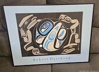 Framed print showing abstract indigenous art with animal motifs in black, blue, and cream hues with artist's name visible.
