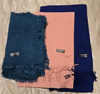 Three pashmina scarves folded side-by-side showing colors and texture variations with labels visible.