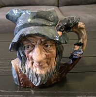 Front and side view of Royal Doulton Rip Van Winkle Toby Jug showing detailed facial features, crow on handle, and small figure below crow.