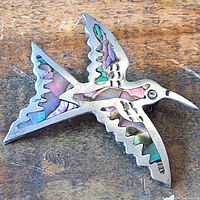 Top side of the silver bird brooch showing abalone inlay with iridescent colors and detailed wing shapes.