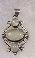 Close-up of silver pendant with three oval translucent cabochon stones set in decorative frame