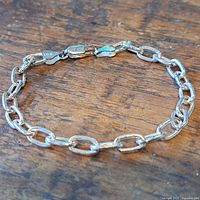 Close-up of the polished sterling silver link bracelet laid flat on wooden surface showing oval chain links and lobster clasp.