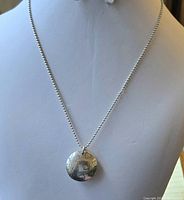 Front view of the necklace on display showing the large round pendant with etched hearts and bead chain.