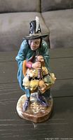Front view of the figurine showing man playing pipe with theatrical masks around waist and feathered black hat.