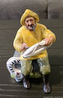 Front view of vintage Royal Doulton ceramic figurine 'The Boatman' depicting a seated fisherman in yellow raincoat and hat.