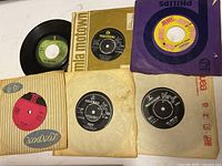 Collection of 45 RPM singles visible with various labels and paper sleeves including The Beatles on Parlophone label.