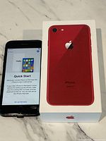 Red iPhone 8 on quick start setup screen with visible crack on lower right of the screen next to original box.