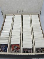 Long white box of Upper Deck hockey cards organized in four rows separated by cardboard dividers. Cards mostly face down showing white backs, some face up previewing player portraits.